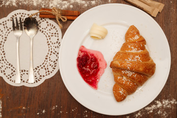 It lies on a plate with croissants, jam and butter, sprinkled with powdered sugar
