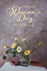 Beautiful flowers in vase on table against color background. Text INTERNATIONAL WOMAN'S DAY, 8TH MARCH