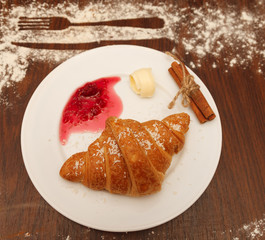 It lies on a plate with croissants, jam and butter, sprinkled with powdered sugar