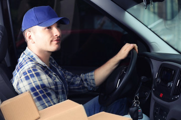 Young male deliverer with boxes sitting in car