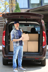 Young male deliverer loading boxes into car