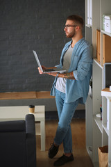 Young man holding laptop standing near wall