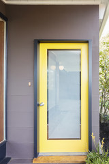 Yellow framed frosted glass door entry surrounded by greenery.