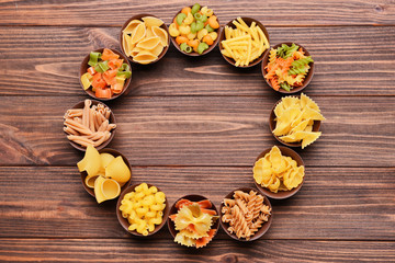 Different kinds of pasta in bowls on wooden background