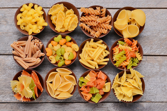 Different kinds of pasta in bowls on wooden background