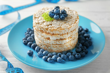 Round rice crispbreads with blueberries and measuring tape on table, closeup