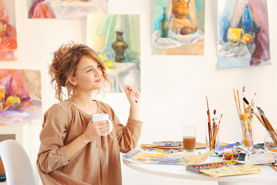 Young female artist drinking coffee in studio