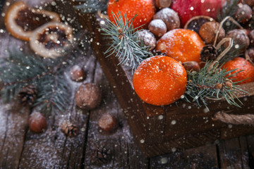 Fototapeta na wymiar Christmas New Year card. Tangerines,Nuts,Pomegranate,Citrus,Tree Branches in a wooden box.Festive Background.Drawn Snowfall.Vintage style.selective focus.