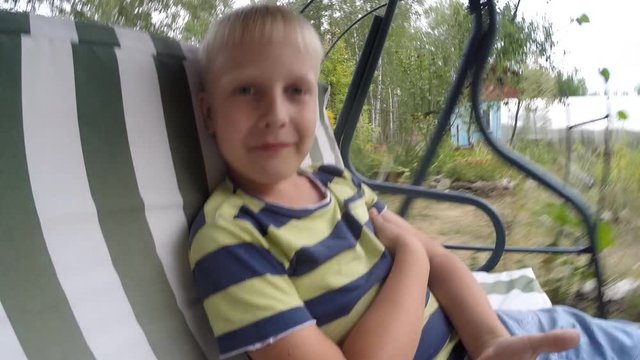 Little blond boy (7 years old) says, swinging on the swing in the summer nature 