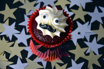 Cupcake with black mustache and whipped white cream on top. Movember cancer awareness in November month. Movember campaign against prostate cancer. Gold and silver stars in the background.