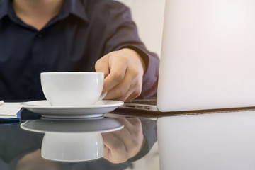 Business man holding cup of coffee and using laptop computer