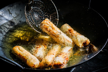 Tasty spring rolls frying in hot oil