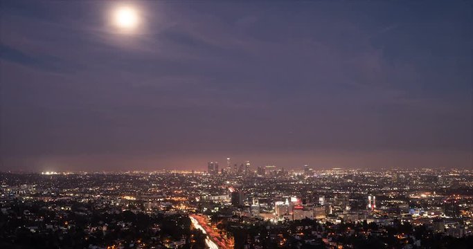 Full moon rising over the bright city lights and traffic with view of The Los Angeles Skyline time lapse video