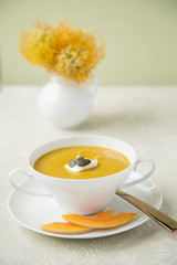 Kuerbissuppe in einer Suppentasse mit Kuerbisspalten, Creme Fraiche und Kuerbiskernen