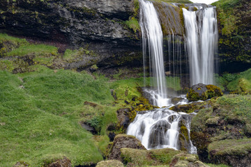 Hidden waterfall between rocks and green grass at Snæfellsnes, Iceland