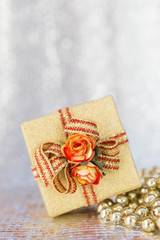 Christmas present on shiny golden beads, gold gift box and paper rose flower on silver background