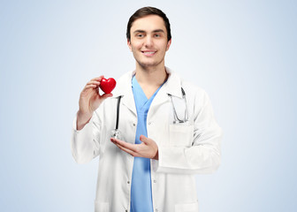 Young doctor with red heart on light blue background