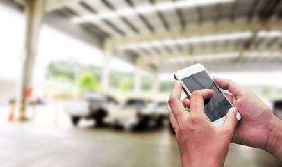 Hand hold and touch screen smart phone on blurred image of park car concept for design.