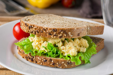 Sandwich with scrambled eggs, salad and tomato on white plate. Close up view