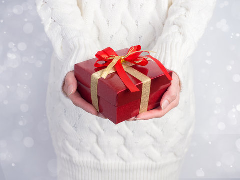 Celebrate year 2017.Close up shot of female hands holding a gift box and nice ribbon. Gift box color  in the hands of a woman wearing a knitted hat sweater on white snow , snowflake background.