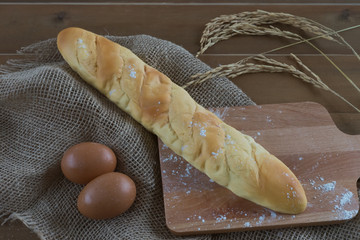 loaf pice of bread on wooden breadboard on wooden table and ear of rice golden color in morning sunrise / bread on breadboard