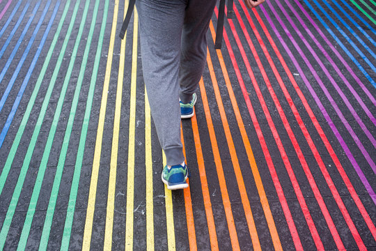 Low section of man walking on rainbow crosswalk