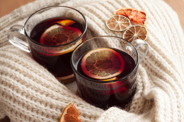 Seasonal and holidays concept . Christmas mulled wine with beautiful orange slices inside the glass , covered with warm white scarf . Very warm and cozy atmosphere