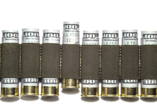 Row of 12 caliber shotgun shells loaded with hundred us dollar bills in bandolier.  One shell is moved upward. The concept of the power of money. Isolated on white background.