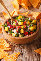 Mexican Food: salsa with mangoes, peppers, cilantro and onion close up in a bowl and nachos. vertical