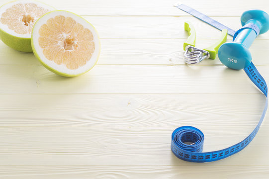 Ripe sliced sweetie and tools for workout, dumbbell, expander and measuring tape on a yellow wooden background. The concept of a healthy, athletic lifestyle.