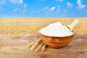 Fototapeta na wymiar flour in bowl on wheat field background
