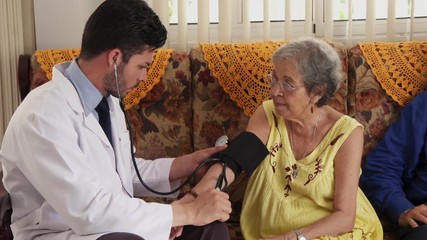 Doctor at work in medical clinic, measuring blood pressure of old woman. Worker in hospital for seniors. Hispanic man working in hospice with elderly people, health care staff, professional occupation