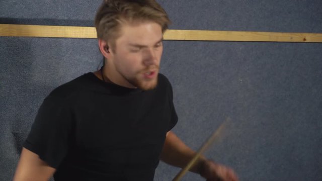 Portrait handsome young drummer emotionally playing on drum set. Music player in pop or rock band wearing in black t-shirt on run-through indoors