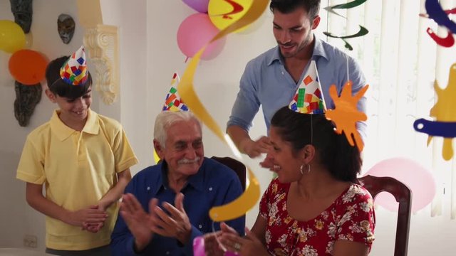 Group of old friends and family celebrating senior man birthday in retirement home. Happy elderly people having fun during party. Grandfather blowing candles on cake and smiling. Slow motion
