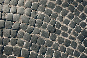 Dark paving stone roadway. Urban stone paving stones. Stone road texture. Ancient a cobblestone road. The fragment of a pavement.