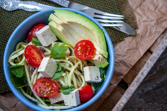 Vegan zucchini pasta in a bowl with tofu, tomatoes, avocado and herbs. Perfect for the detox diet or just a healthy meal.  Love for a healthy raw food concept.