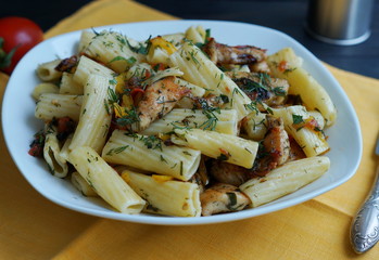 tortiglione pasta with chicken in a sauce of tomato, pepper and parsley on a yellow background 