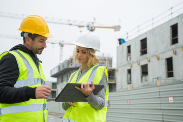 builders in hardhat with tablet at construction