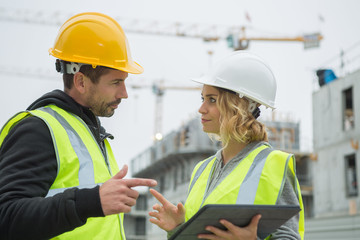 builders in hardhat with tablet at construction