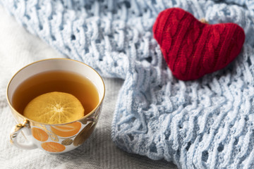 Fototapeta na wymiar knitted red heart on knitted wool blue and gray shawl with golden cup of tea with lemon