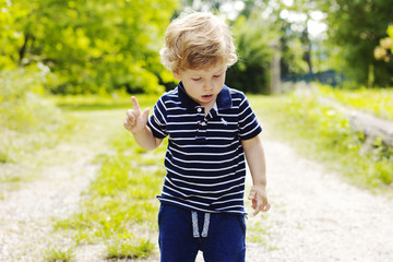 A little boy walks outdoors. The kid walks on the green grass.
