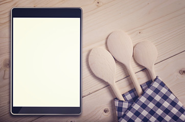 Tablet on wooden surface and serving spoons.