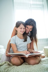 Mother and daughter reading book on bed
