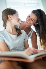 Mother and interacting daughter while reading book on bed