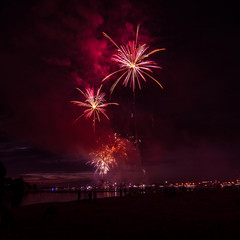 People watching colorful fireworks above the river