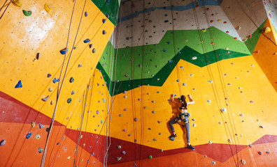 Confident woman climbing up the orange wall in gym