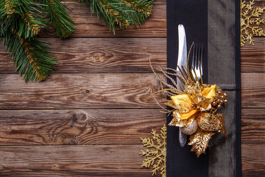 Christmas table place setting decorated black napkin with fork and knife, gold flower and snowflakes and christmas pine branches.