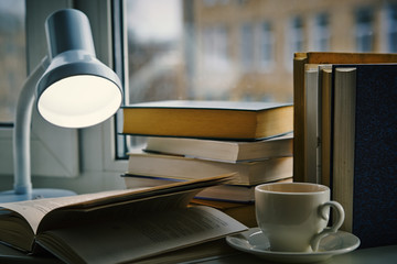 A cup of tea, open book under the lamp on the window