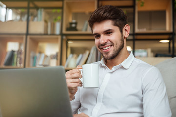 Cheerful businessman drinking tea while looking at laptop.