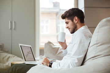 Obraz premium Joyful businessman drinking tea while looking at laptop.